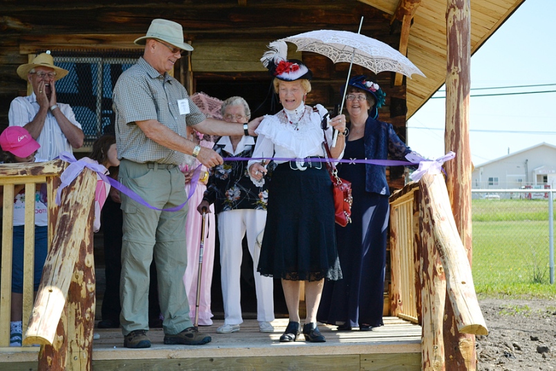 Photo by Carl BR Johnson -- Charlie Parslow holds the ribbon for Doris Cox to cut at the newly acquired trapper's cabin at the Walter Wright Pioneer Village.