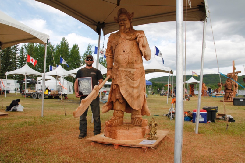 Photo by William Stodalka -- Jeff Samudosky of Gig Harbour, Washington, U.S., poses with his first place plaque next to a carving of Guan Gong at the Chetwynd Chainsaw Carving Competition.